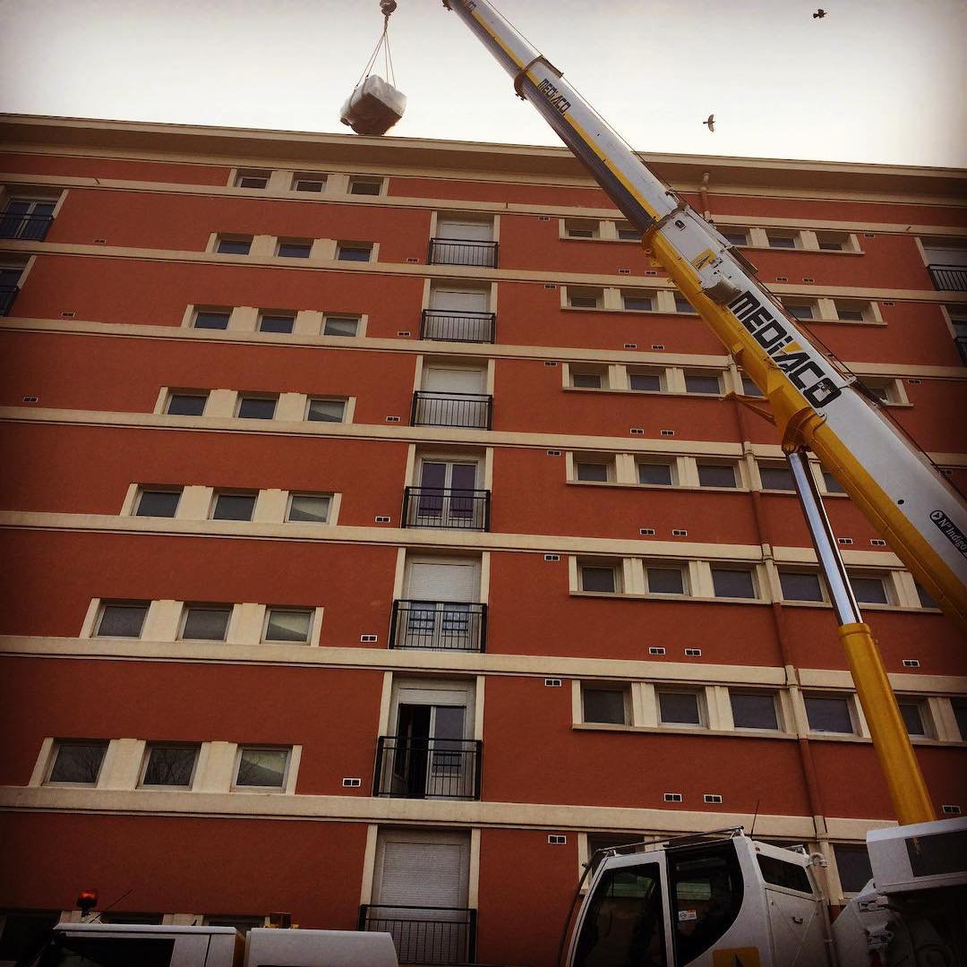 Crane déplaçant des matériaux de rénovation énergétique sur un bâtiment résidentiel.