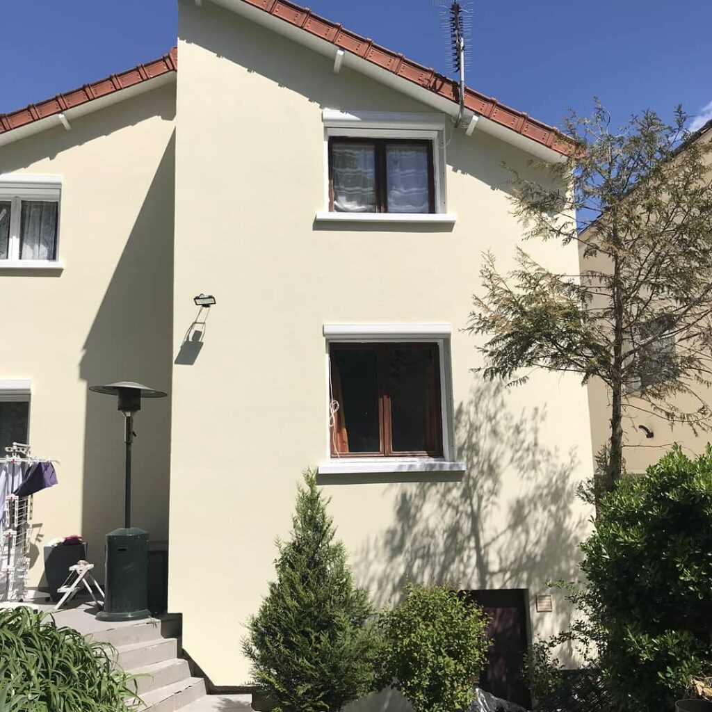 Maison jaune avec fenêtres et plantes, rénovation énergétique en cours