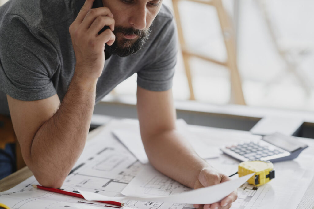 Homme au téléphone avec des plans AD VALIDEM; Rénovation énergétique; Audit énergétique.